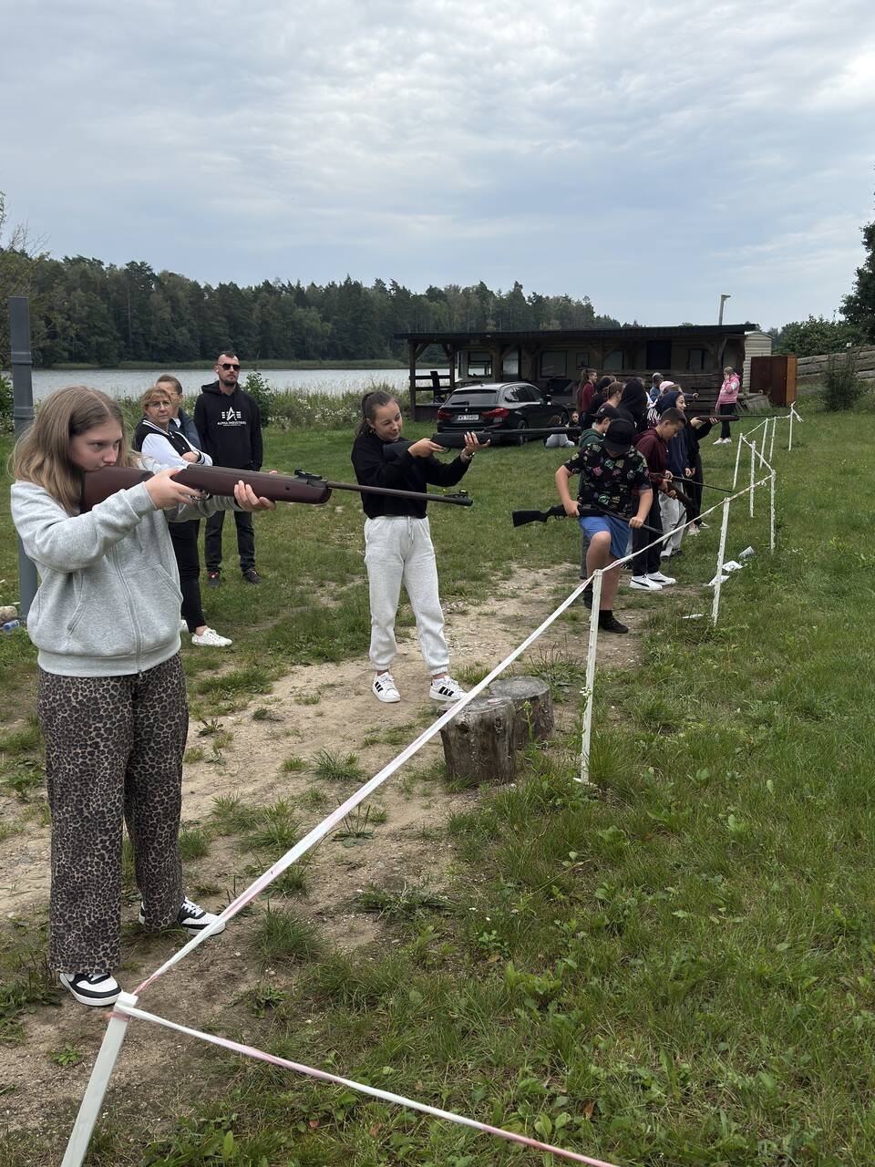 Młodzież uczestniczy w&nbsp;zajęciach strzeleckich na&nbsp;świeżym powietrzu, ćwicząc celność z&nbsp;broni sportowej.