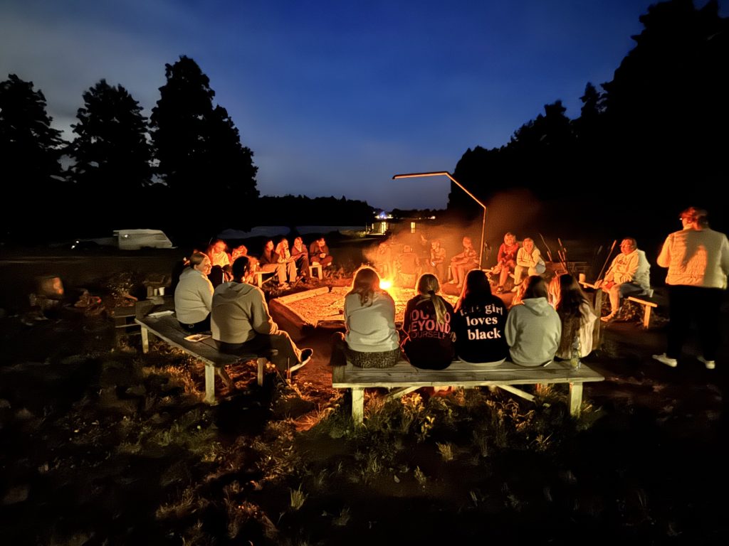 Grupa ludzi siedzi wok&oacute;ł ogniska w&nbsp;nocy, ciesząc się wsp&oacute;lnym czasem i&nbsp;atmosferą.