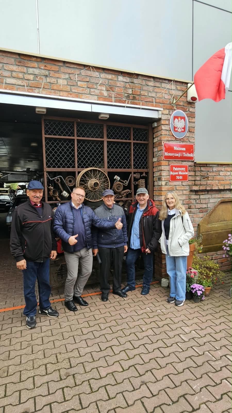 Na zdjęciu widać pięcio osobową grupę osub pozujących do zdjęcia przed muzeum motoryzacji i&nbsp;techniki 