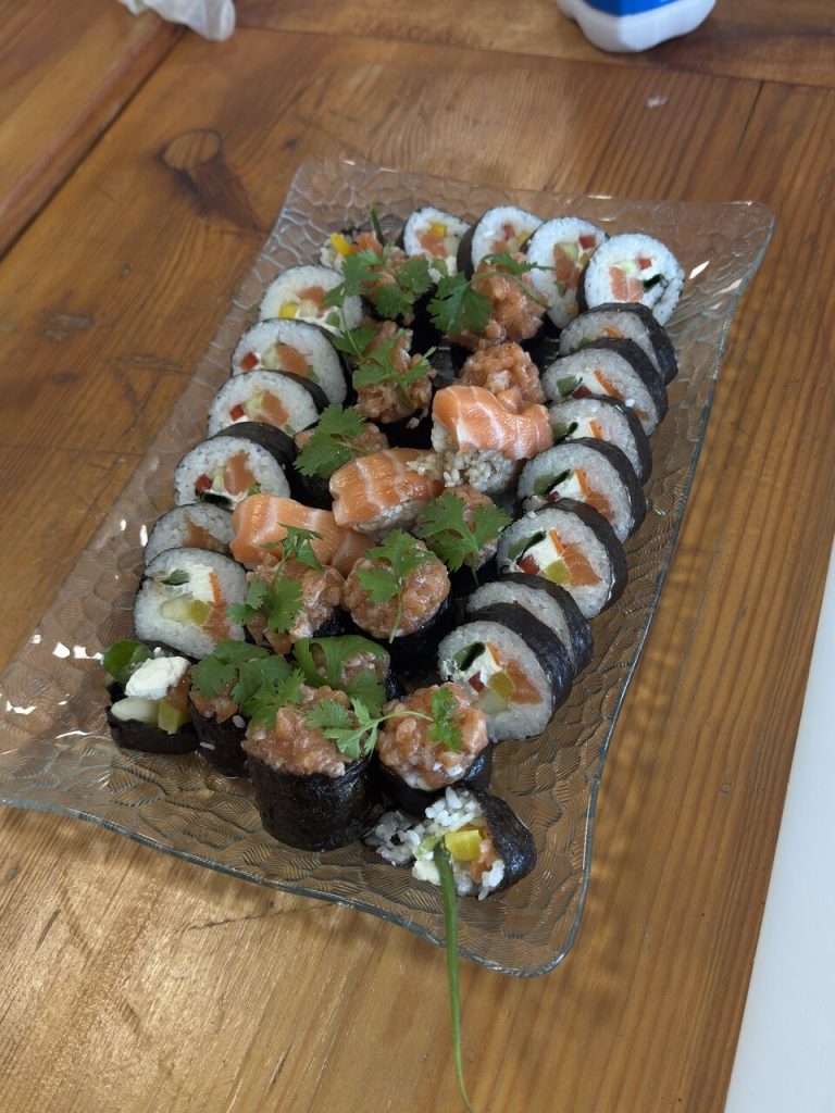 Talerz sushi z&nbsp;r&oacute;żnorodnymi rolkami, w&nbsp;tym z&nbsp;łososiem, warzywami i&nbsp;kolendrą, na&nbsp;drewnianym stole.
