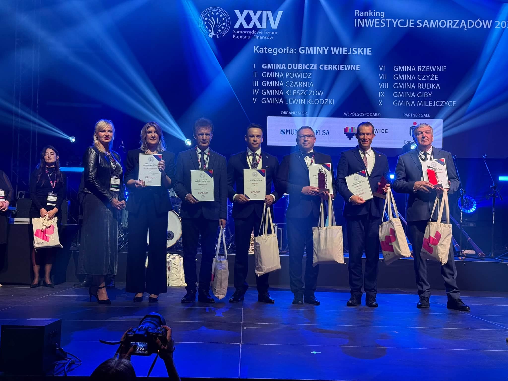 Na zdjęciu widać laureat&oacute;w rankingu inwestycyjnym &bdquo;Wsp&oacute;lnoty&rdquo;. trzymaj oni dyplomy i&nbsp;statułetki. wszyskto jest podświetlone na&nbsp;niebiesko 