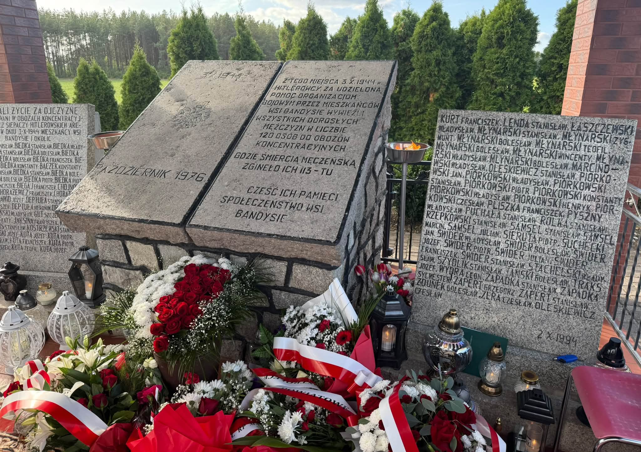 Pomnik mieszkańc&oacute;w wsi Bandysie wywiezionych 3 października 1944 roku do oboz&oacute;w koncentracyjnych. Przed tablicami z&nbsp;nazwiskami ofiar złożono biało-czerwone wieńce i&nbsp;zapalono znic